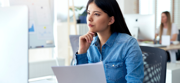 disciplina no trabalho, mulher olhando fixamente a tela de computador, enquanto segura papel na mão e na outra segurando o queixo