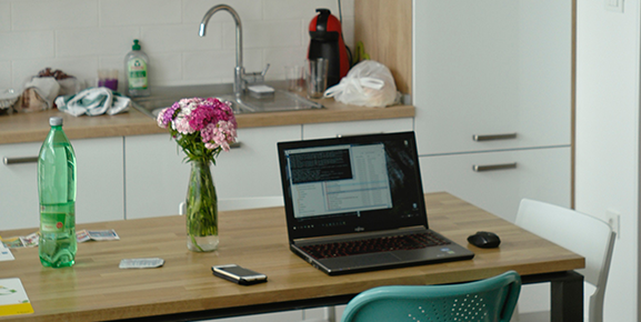 home office, computador ligado, em cima da mesa, celular, flores, garrafa de agua