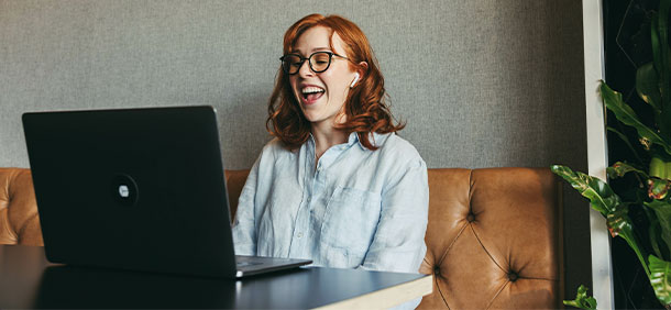 mulher sorrindo com fone de ouvido enquanto trabalha em seu notebook em uma mesa