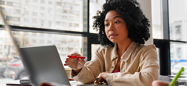 mulher concentrada em seu laptop aparentando analisar ou discutir ideias degura uma caneta sugerindo que esta engajada usando a criatividade e a produtividade no trabalho