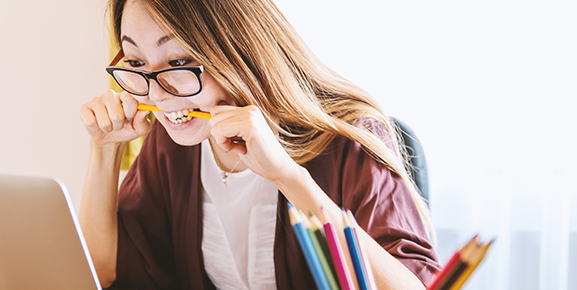 mulher de óculos colocando um lapis na boca enquanto olha para o notebook