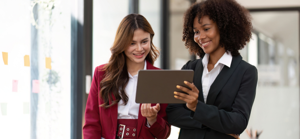 lider e gestora sorrindo e alinhadas diante de um tablet união entre gestão e liderança para decisões estratégicas com confiança