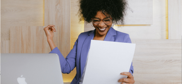 mulher comemorando uma conquista com expressão de entusiasmo e satisfação diante do computador