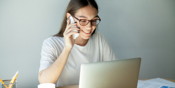 home office produtivo, mulher trabalhando em home office, falando em telefone em frente ao notebook, sorrindo