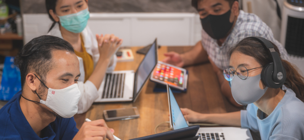 equipe trabalhando em tempos de crise usando máscaras em um ambiente colaborativo com laptops e tablet