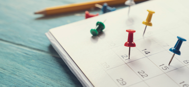 A imagem retrata um calendário com alfinetes coloridos marcando diferentes datas, representando visualmente a importância do planejamento
