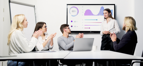 homens e mulheres sentados a mesa enquanto mulher em pé mostrando no painel gráfico de resultado do feedback