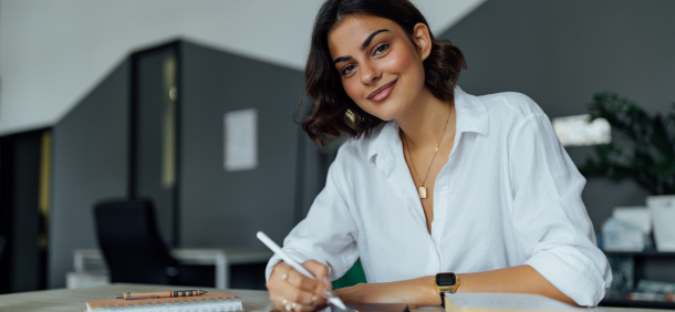 imagem mostra uma mulher jovem sentada à mesa em um ambiente de trabalho moderno e bem iluminado