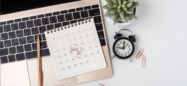 Calendário sobre notebook com relógio e planta, representando gestão do tempo, planejamento de tarefas e organização da rotina profissional.